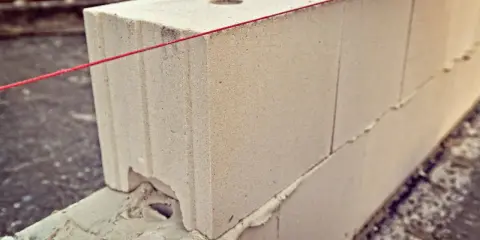 Budowa muru z bloczków suporeks. Czerwona nić wyznacza linię, pomagając określić, ile suporexu na m2 potrzeba do budowy.