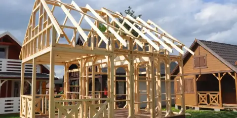 Konstrukcja domu szkieletowego 70m2 w trakcie budowy. Widać drewniany szkielet ścian i dachu, taras oraz sąsiednie budynki.
