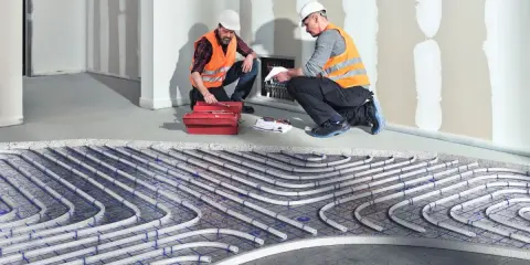 Dwóch fachowców montuje instalację ogrzewania sufitowego wodnego. Rury systemu ułożone są na siatce.