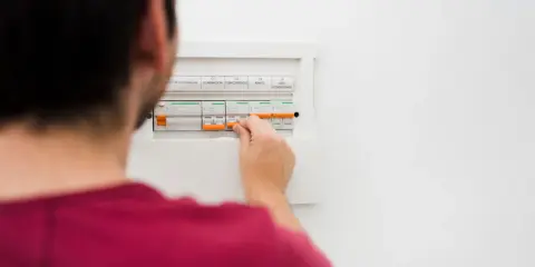 Mężczyzna manipuluje wyłącznikami w skrzynce elektrycznej, co może być związane z tym, jak obliczyć zużycie prądu.