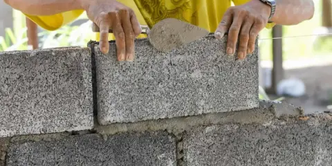 Murarz kładzie betonowy bloczek na zaprawie, używając kielni.