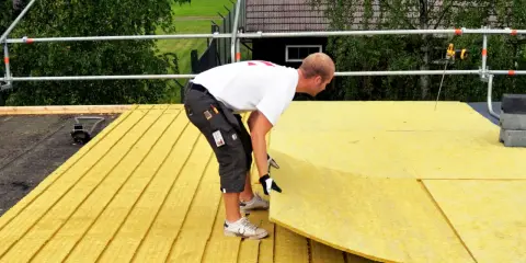 Pracownik układa płyty izolacyjne na dachu płaskim. Zapewnia to skuteczną izolację termiczną budynku.