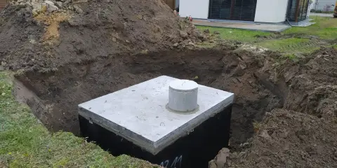 Betonowy zbiornik w wykopie, przygotowany na odpływ z rynny do ziemi.