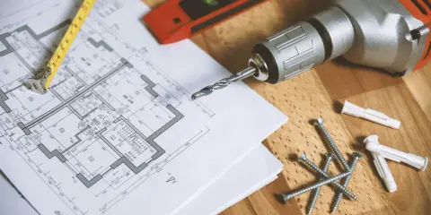 Narzędzia budowlane i plan mieszkania. Zastanawiasz się, jak obliczyć metry kwadratowe ściany? Ten obrazek pokazuje, że potrzebujesz planu i miarki.
