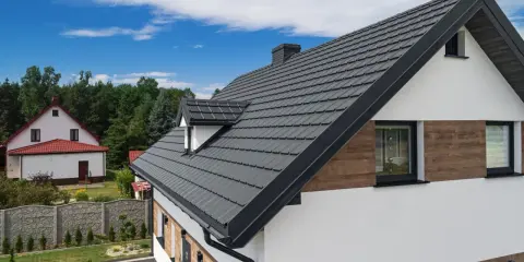 Nowoczesny dom z grafitową elewacją i dachówką, otoczony zielenią.