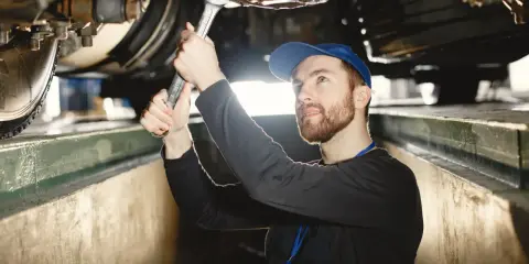 Mechanik z kluczem pracuje pod samochodem, sprawdzając wymiary kanału samochodowego.