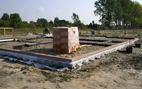 Stan zero budynku: fundamenty z cegły i betonu, stos materiałów budowlanych.