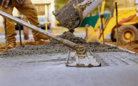 Pracownik wylewa beton, wyrównując go narzędziem. W tle koparka. Beton można lać do ok. 30°C.