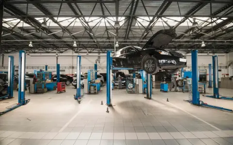 Nowoczesny projekt warsztatu samochodowego. Na podnośnikach stoją auta, mechanicy pracują.