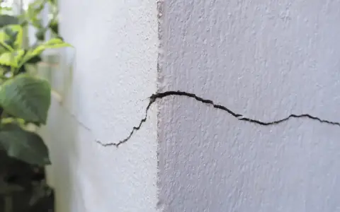 Widoczne pęknięcia na rogu białego budynku, świadczące o jego osiadaniu.