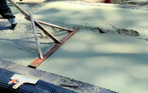 Pracownik wyrównuje świeży beton, sprawdzając, jaka grubość chudziaka jest potrzebna. Narzędzie do zacierania betonu w akcji.