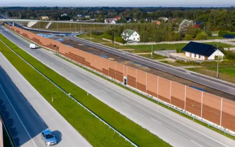 Długa, brązowa ekran akustyczny od sąsiada chroni domy przed hałasem drogi szybkiego ruchu.
