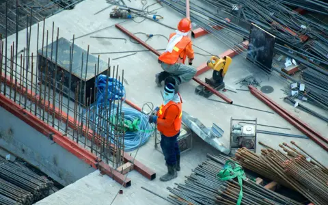Budowa domu to proces, który wymaga czasu i pracy. Na placu budowy widać robotników i materiały.