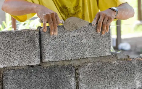 Murarz układa bloczek betonowy, dbając o jego wymiary i równość.