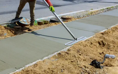 Pracownik wygładza świeży beton na chodniku. Jaki beton na wieniec? Ten budowlany jest idealny do takich prac.