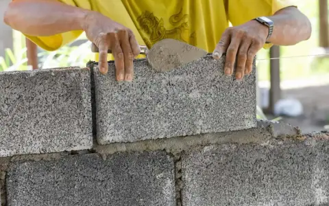 Murarz kładzie betonowy bloczek na zaprawie, używając kielni.