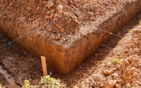Wyznaczone wykopy pod fundamenty, z widocznymi nićmi wyznaczającymi linie i drewnianym palikiem.