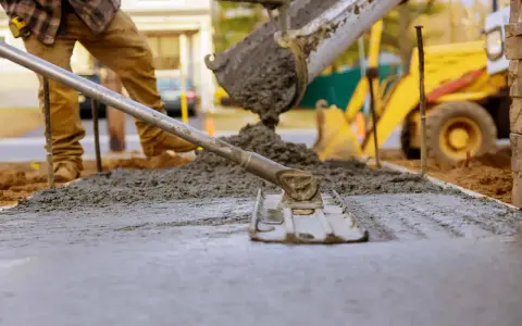 Pracownik wylewa beton, który będzie długo schnął w temperaturze 5 stopni. W tle koparka.