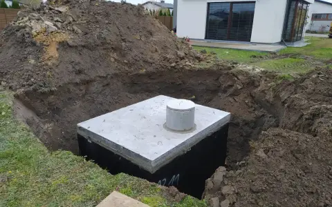 Betonowy zbiornik w wykopie, przygotowany na odpływ z rynny do ziemi.