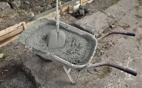 Taczka z betonem i łopatą czeka na wylanie zbrojenia ławy fundamentowej.