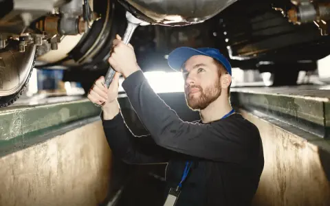 Mechanik z kluczem pracuje pod samochodem, sprawdzając wymiary kanału samochodowego.