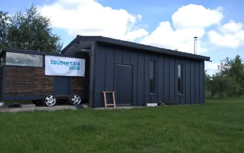 Mobilny garaż na zgłoszenie, z banerem "Zbuduj sam dom", stoi na trawie.