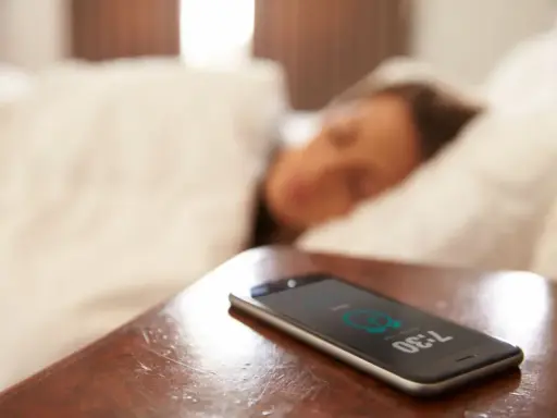 Telefon na stoliku nocnym pokazuje 7:30, budząc śpiącą osobę. To typowy widok na poziomie zero budynku, gdzie zaczyna się dzień.
