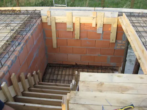 Budowa schodów zabiegowych betonowych. Widać zbrojenie, ceglane ściany i drewniane szalunki.
