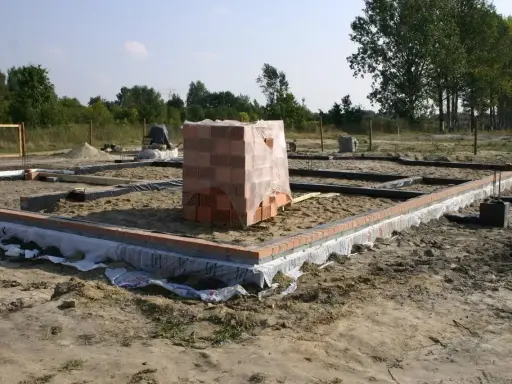 Stan zero budynku: fundamenty z cegły i betonu, stos materiałów budowlanych.