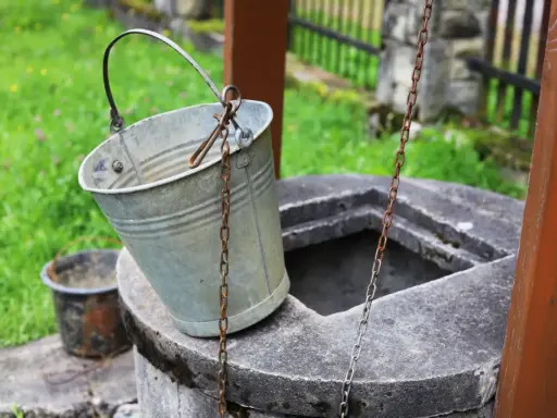 Metalowy wiaderko przy studni, gotowe do pracy. Ktoś zastanawia się, jak wykopać studnię, by mieć własne źródło wody.