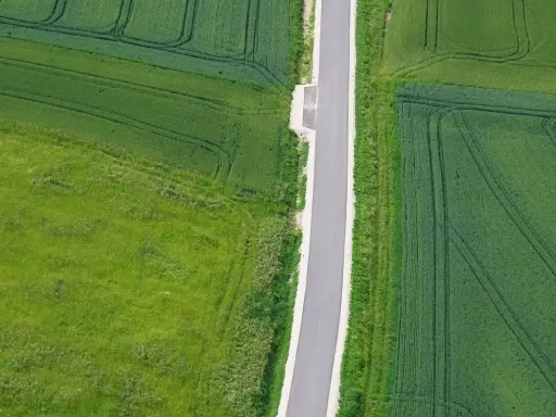 Wąska droga dojazdowa do działki, otoczona polami zielonych zbóż i traw.