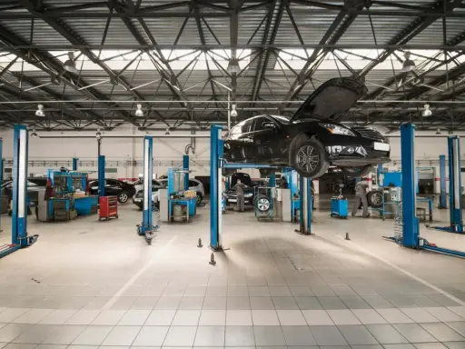 Nowoczesny projekt warsztatu samochodowego. Na podnośnikach stoją auta, mechanicy pracują.