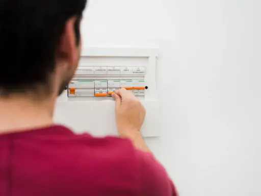 Mężczyzna manipuluje wyłącznikami w skrzynce elektrycznej, co może być związane z tym, jak obliczyć zużycie prądu.