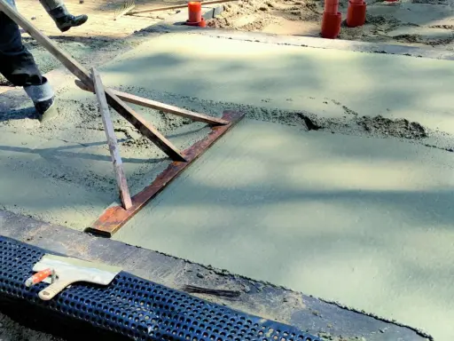 Pracownik wyrównuje świeży beton, sprawdzając, jaka grubość chudziaka jest potrzebna. Narzędzie do zacierania betonu w akcji.