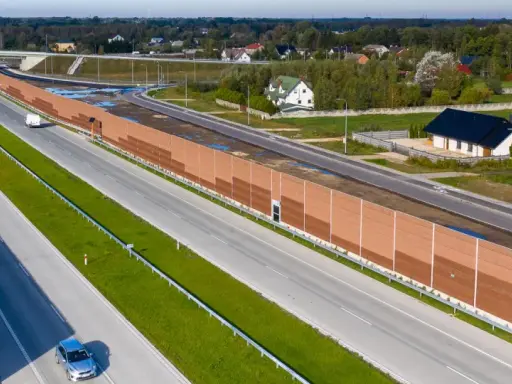 Długa, brązowa ekran akustyczny od sąsiada chroni domy przed hałasem drogi szybkiego ruchu.