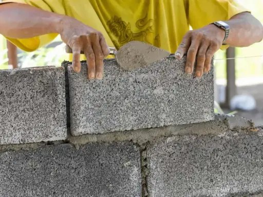 Murarz kładzie betonowy bloczek na zaprawie, używając kielni.