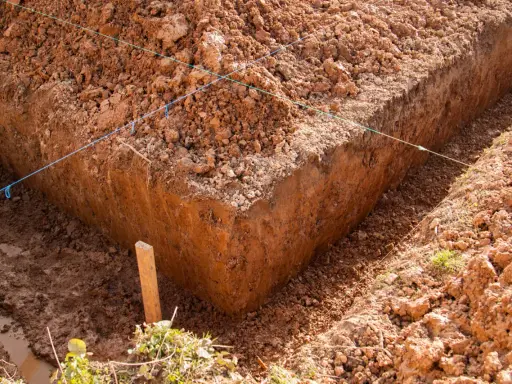Wyznaczone wykopy pod fundamenty, z widocznymi nićmi wyznaczającymi linie i drewnianym palikiem.
