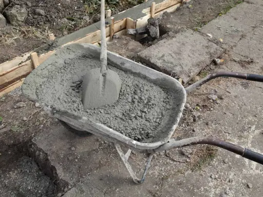 Taczka z betonem i łopatą czeka na wylanie zbrojenia ławy fundamentowej.