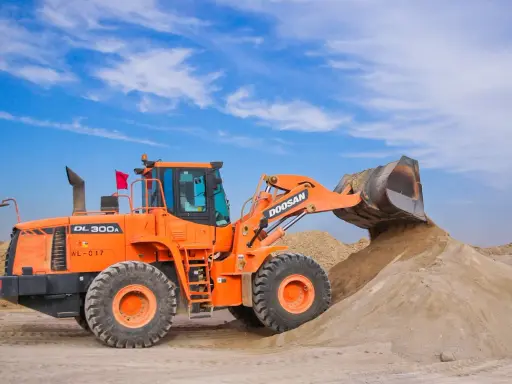 Pomarańczowa ładowarka Doosan DL300A zasypuje kopiec piasku, który może posłużyć jako żwir do betonu.