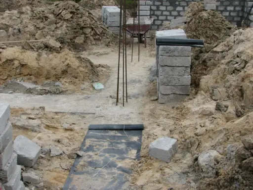 Budowa fundamentu z bloczków betonowych, zbrojenie i wózek widłowy w tle.