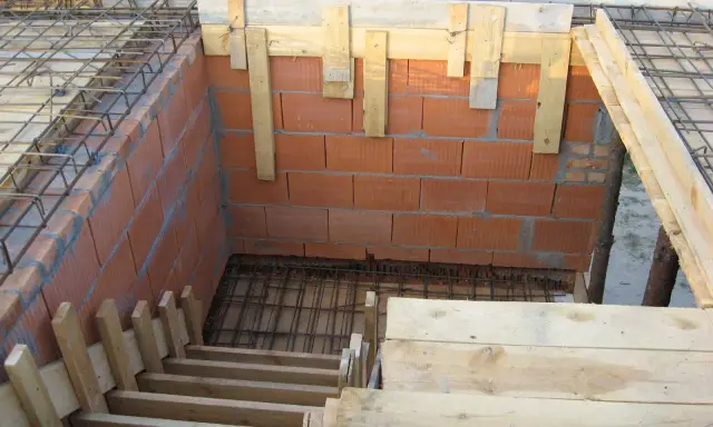 Budowa schodów zabiegowych betonowych. Widać zbrojenie, ceglane ściany i drewniane szalunki.