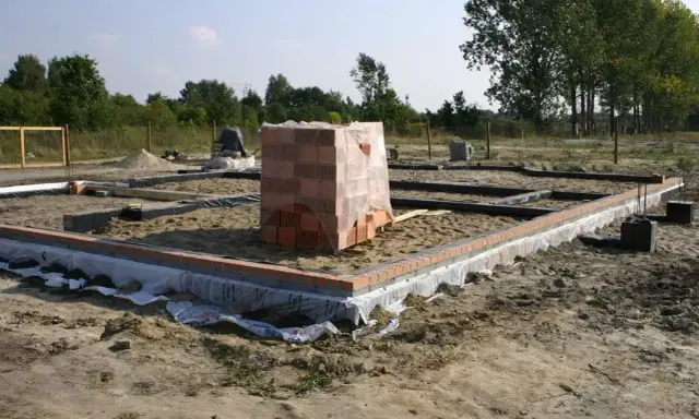Stan zero budynku: fundamenty z cegły i betonu, stos materiałów budowlanych.