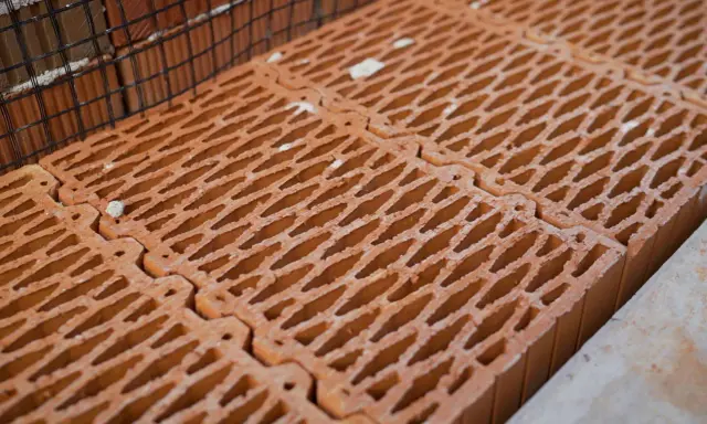 Czerwone pustaki ceramiczne ułożone obok siebie, z siatką zbrojeniową w tle. Zastanawiasz się, ile pustaków na m2 potrzeba do budowy?
