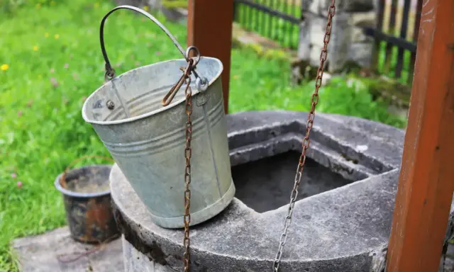 Metalowy wiaderko przy studni, gotowe do pracy. Ktoś zastanawia się, jak wykopać studnię, by mieć własne źródło wody.
