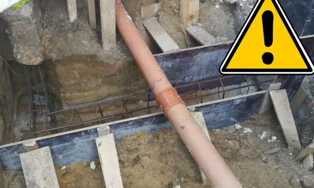 Budowa domu: widoczna rura kanalizacyjna w wykopie, zbrojenie i elementy szalunku.