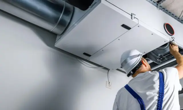 Technik sprawdza wentylację mechaniczną nawiewno-wywiewną. System zapewnia świeże powietrze w budynku.