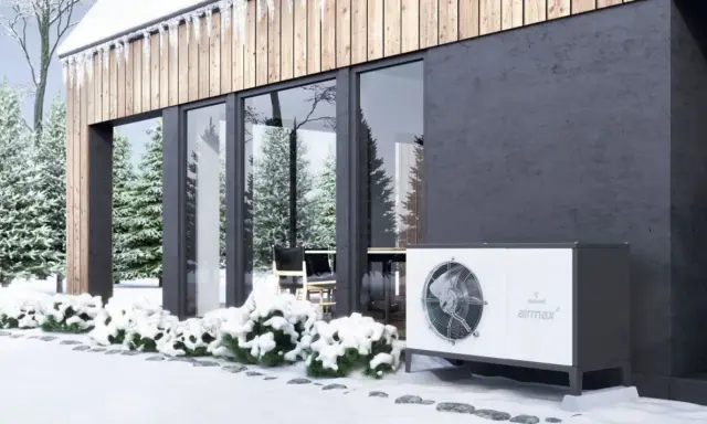 Nowoczesny dom w zimowej scenerii. Obok budynku stoi biała jednostka, która może być alternatywą dla pompy ciepła.