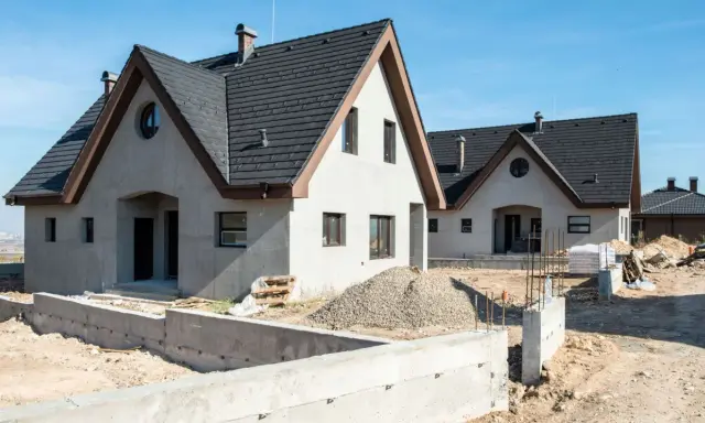 Nowe domy z betonu w budowie, z ciemnymi dachami i jasnymi ścianami, na tle błękitnego nieba.