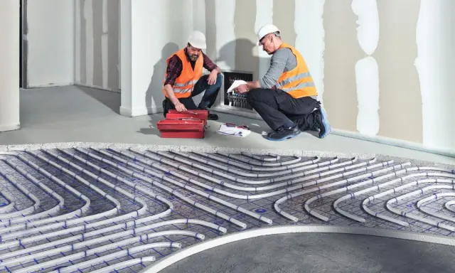 Dwóch fachowców montuje instalację ogrzewania sufitowego wodnego. Rury systemu ułożone są na siatce.