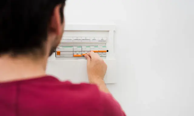 Mężczyzna manipuluje wyłącznikami w skrzynce elektrycznej, co może być związane z tym, jak obliczyć zużycie prądu.